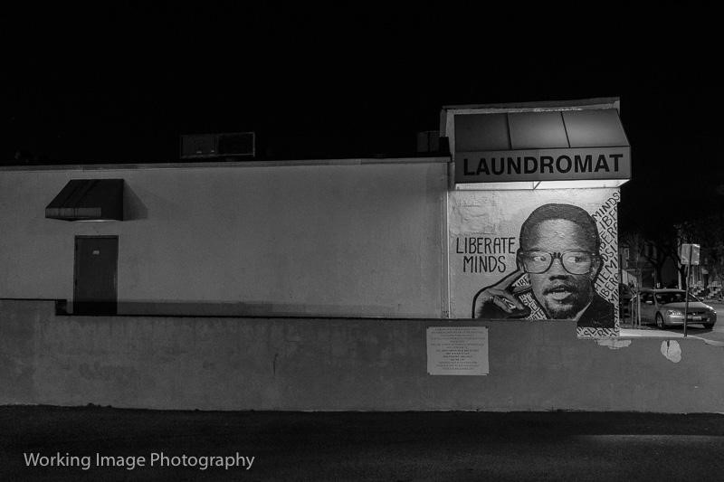 Photo of a laundromat with a mural depicting Malcolm X on the wall with the words liberate minds.