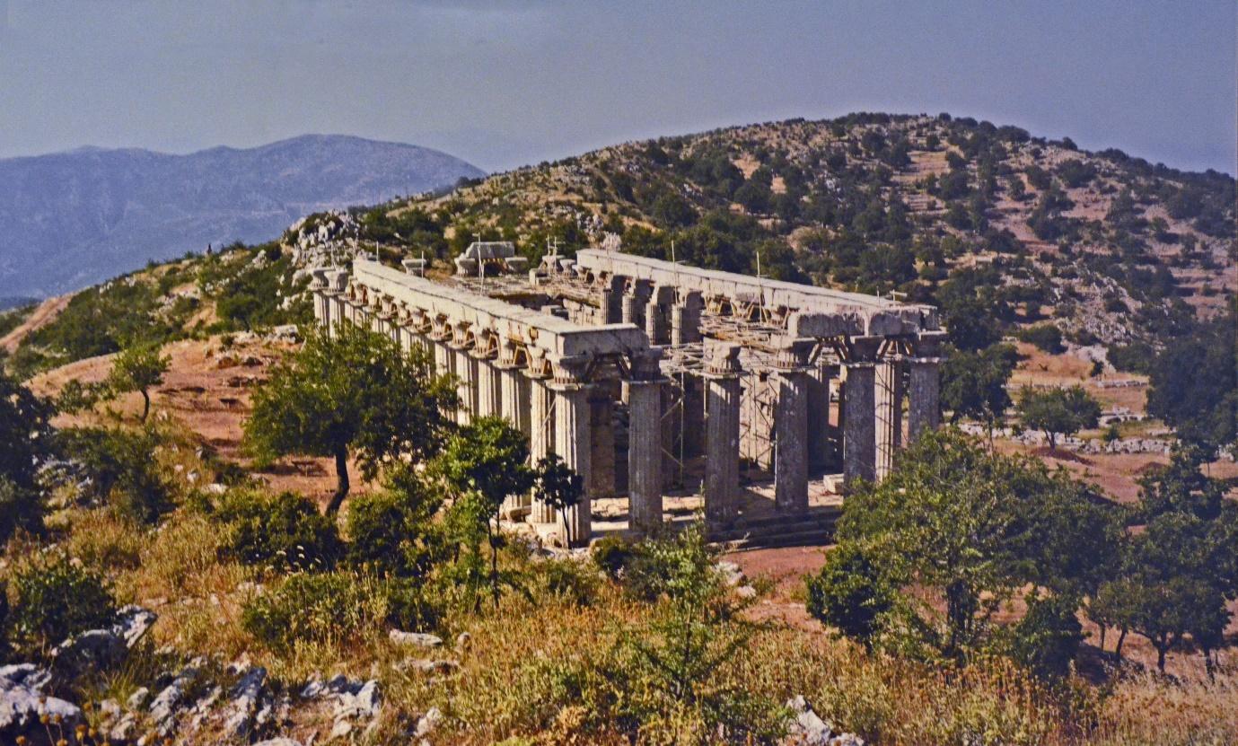 The ruins of the Temple of Apollo, situated on a mountaintop, surrounded by trees.