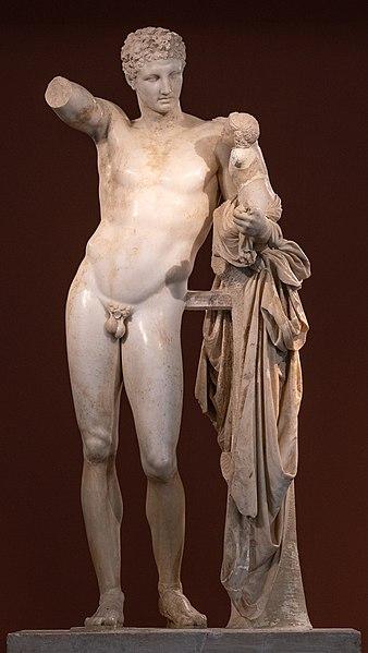 A greyed-white marble statue of Hermes as a young, naked man in posture, holding the baby Dionysus in his left hand. The right arm of the sculpture is missing from the biceps downwards.