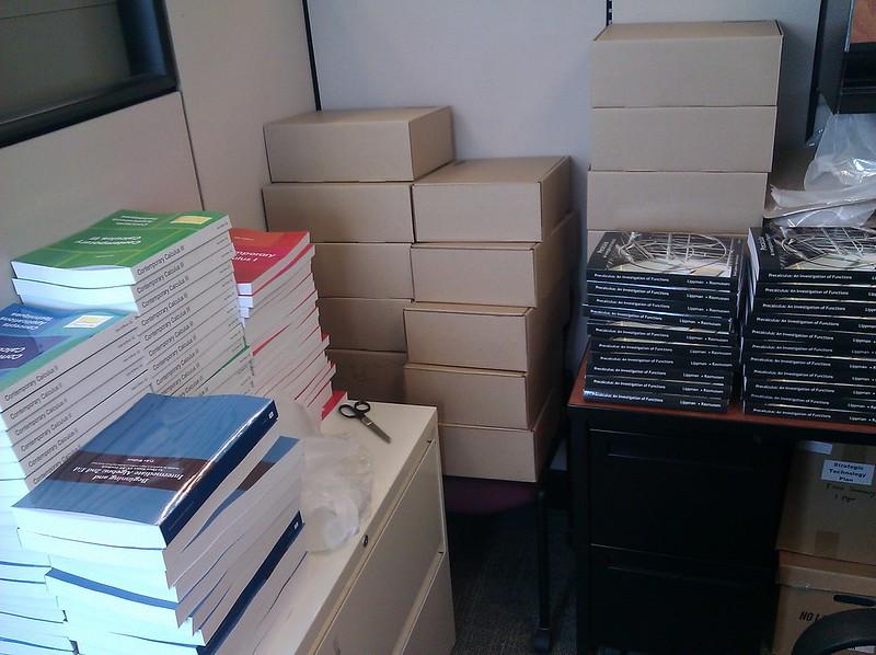 Piles of printed open textbooks on desks and in boxes